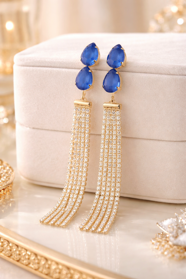 Blue teardrop earrings with gold tassels on a beige jewelry box.