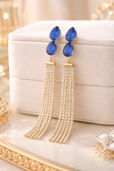 Blue teardrop earrings with gold tassels on a beige jewelry box.