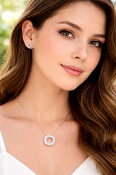 Woman wearing a silver necklace and earrings with a blurred green background
