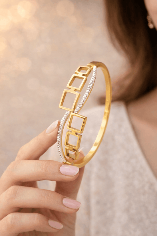 Gold bracelet with geometric design held by a hand against a neutral background