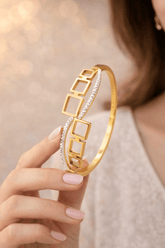 Gold bracelet with geometric design held by a hand against a neutral background