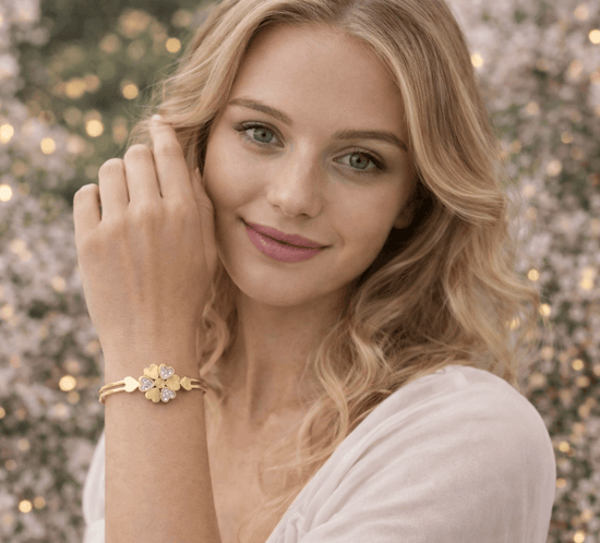 Woman wearing a gold bracelet with a floral design against a blurred floral background