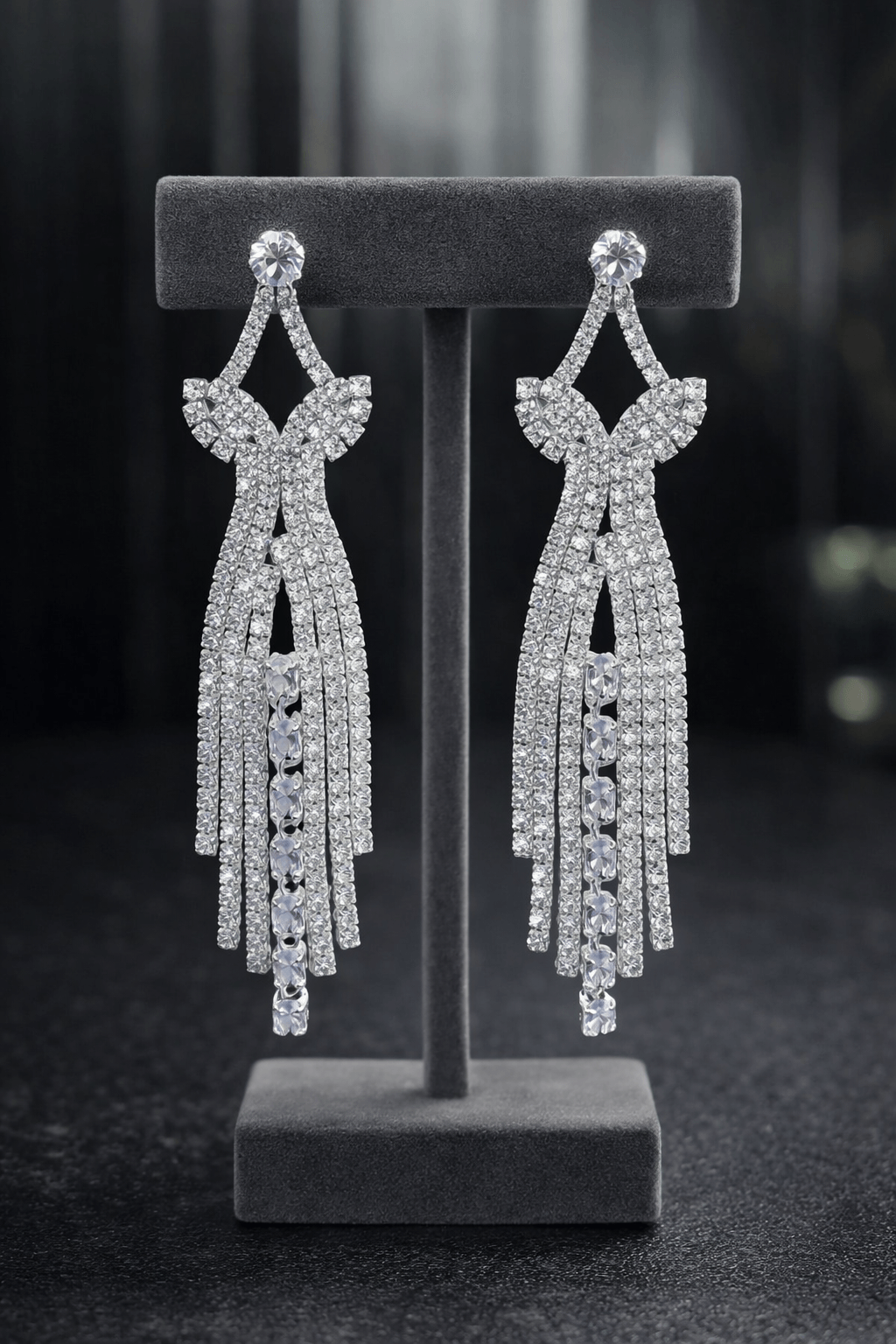 Pair of silver earrings on a gray stand against a dark background