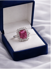 Ring with a pink gemstone in a blue velvet box on a white fabric background