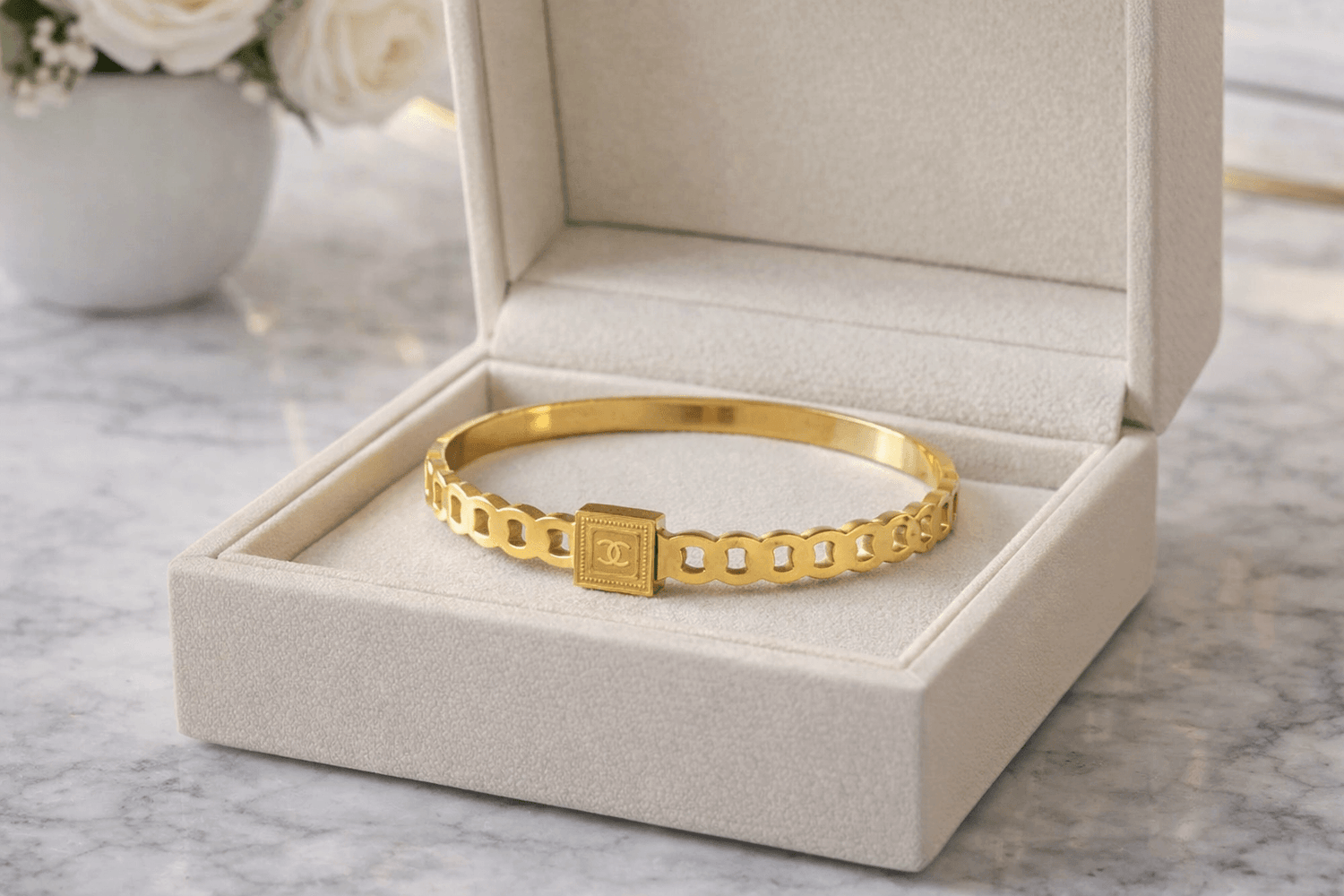 Gold bracelet in an open jewelry box on a marble surface with flowers in the background