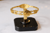 Gold bracelet with Chanel logo on a black stand against a white background