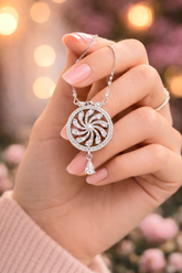 Hand holding a silver necklace with a decorative pendant against a blurred background