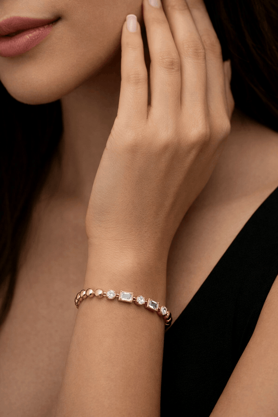 Close-up of a hand wearing a rose gold bracelet with gemstones against a dark background