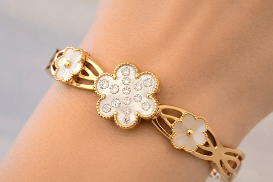 Gold bracelet with floral designs on a wrist against a neutral background