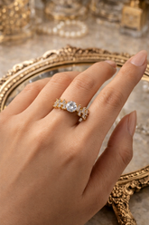 Gold ring with a central gemstone on a hand, with a decorative mirror in the background