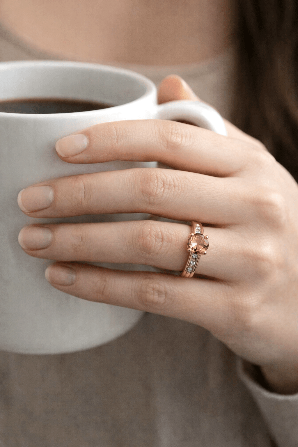 Hand holding a white mug with a gold ring on a neutral background