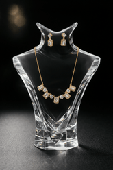 Jewelry set with necklace and earrings on a clear crystal stand against a black background