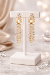Gold chandelier earrings on a white stand with a soft blurred background