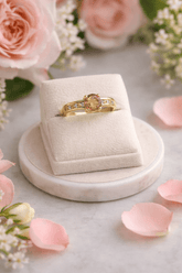 Gold ring with a diamond in a beige box on a marble surface with flowers and petals.