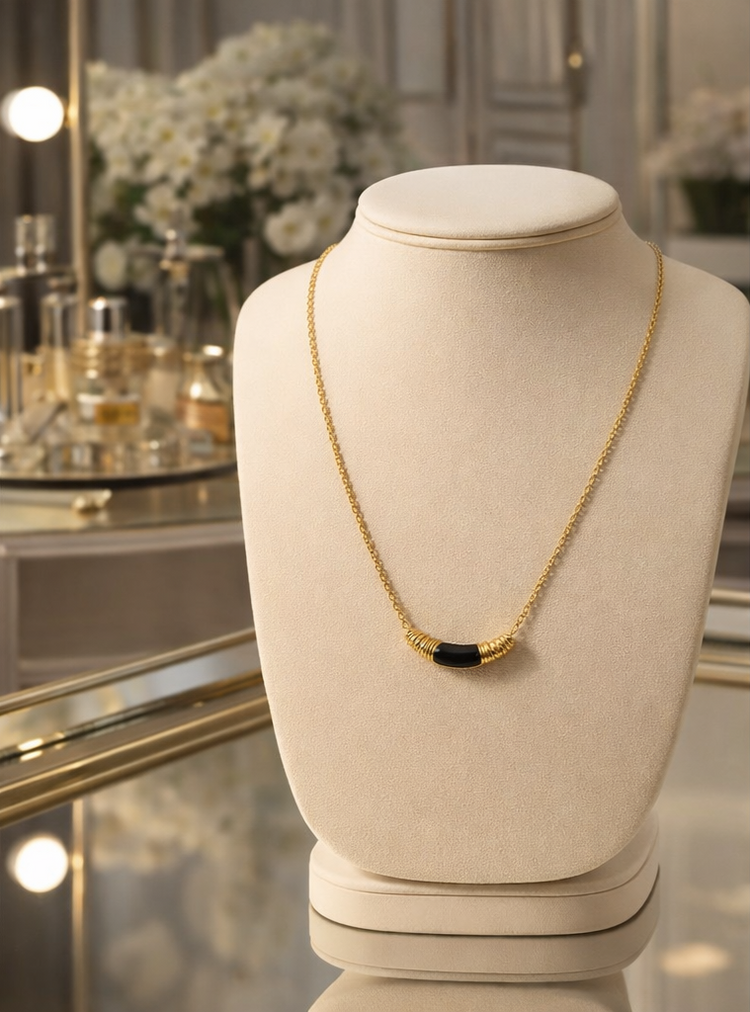 Gold necklace with black stones on a mannequin bust in a decorative setting.