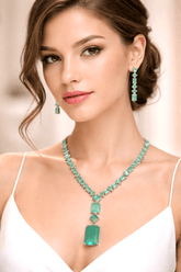 Woman wearing a green emerald necklace and earrings against a neutral background