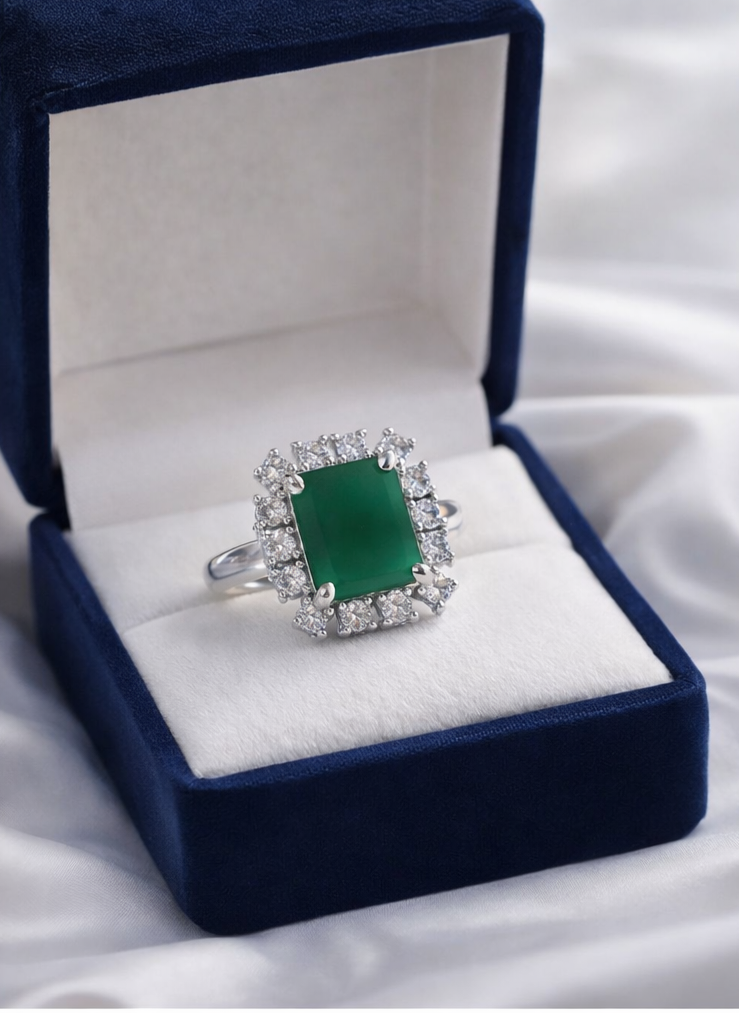 Green gemstone ring with diamond accents in a blue velvet box on a white fabric background