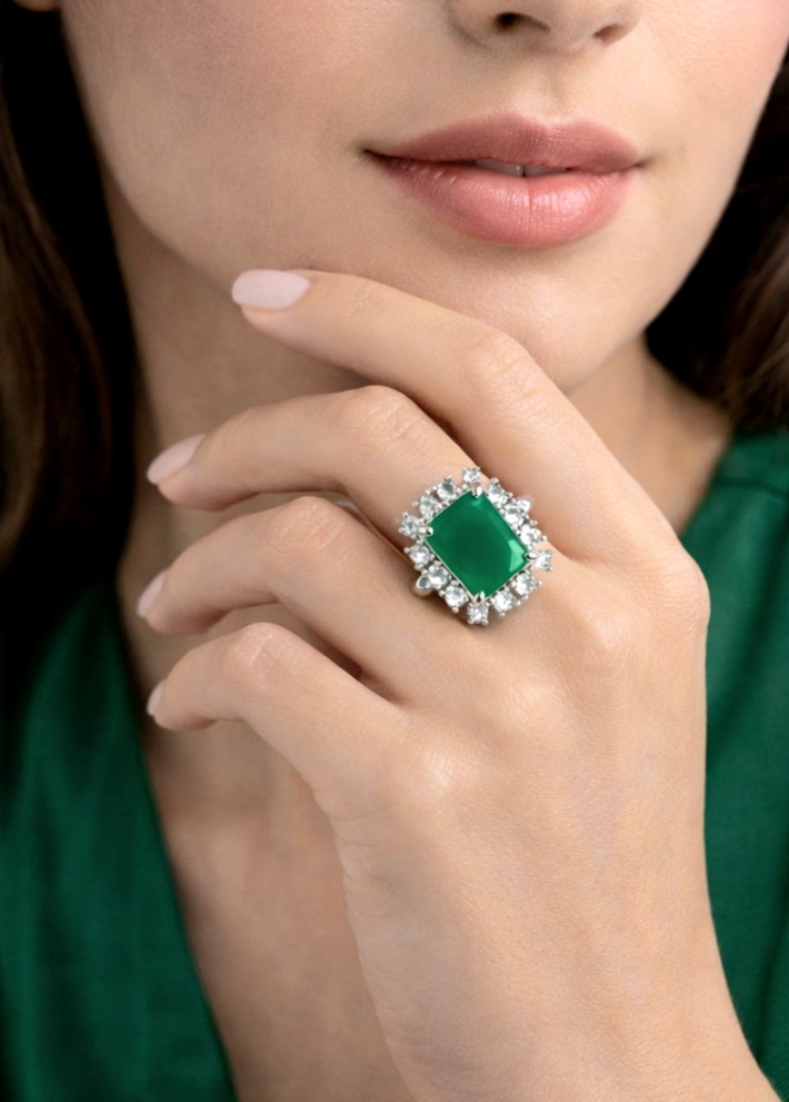 Close-up of a hand wearing an emerald ring with a green background