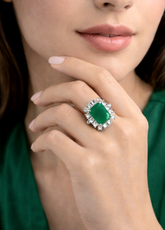 Close-up of a hand wearing an emerald ring with a green background