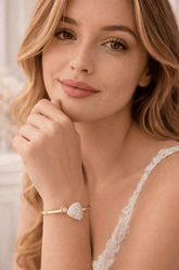 Woman wearing a gold bracelet with a heart-shaped charm against a neutral background