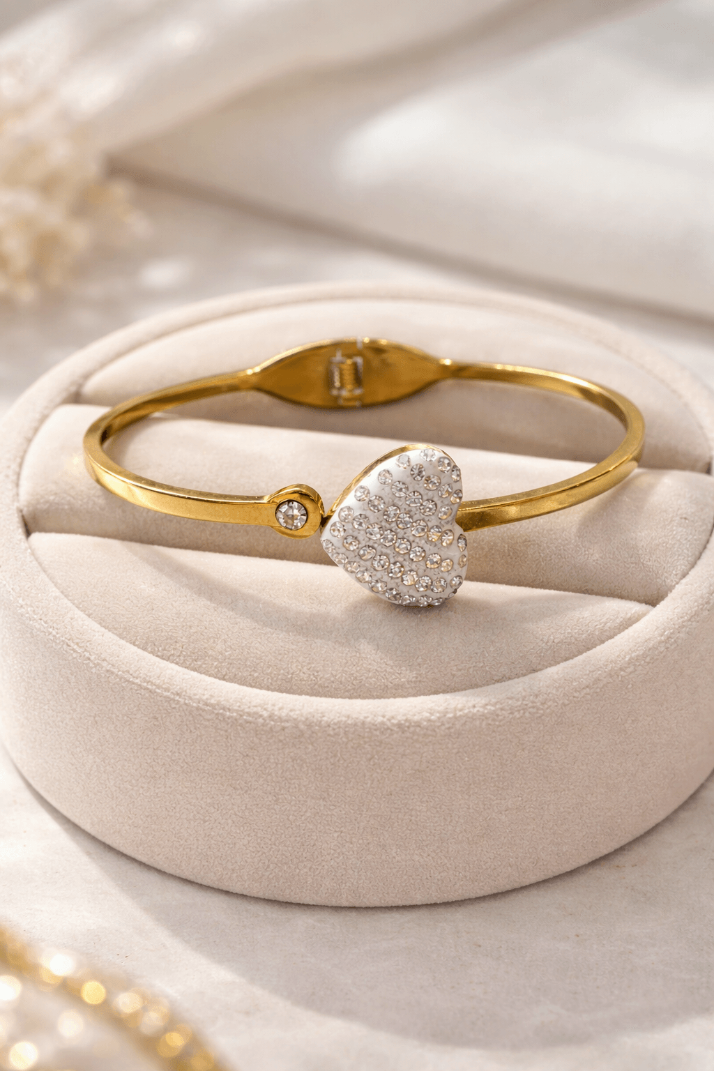 Gold bracelet with a heart-shaped diamond charm on a beige cushion