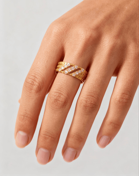 Gold ring with diamonds on a finger against a neutral background