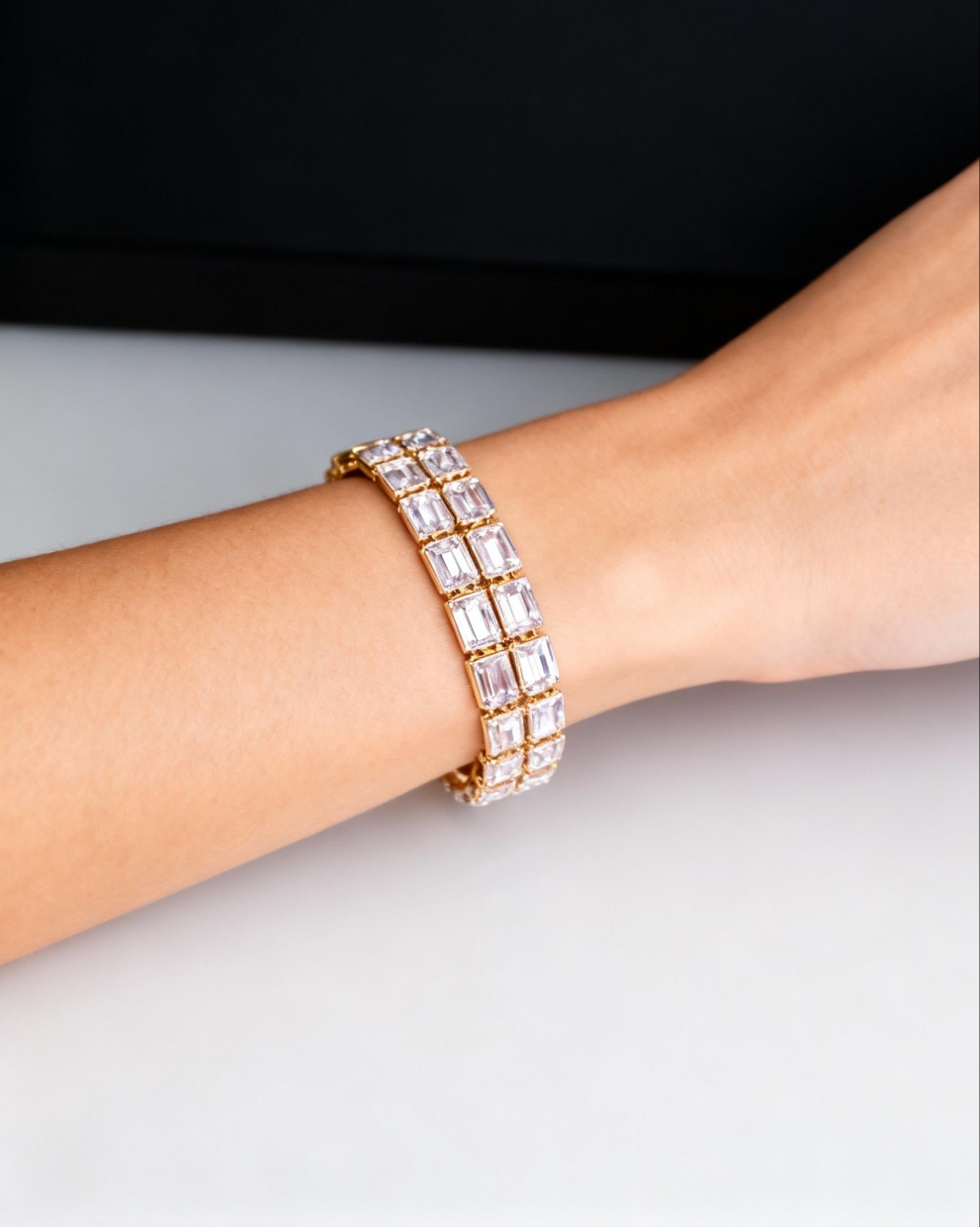Gold bracelet with clear stones on a wrist against a black background