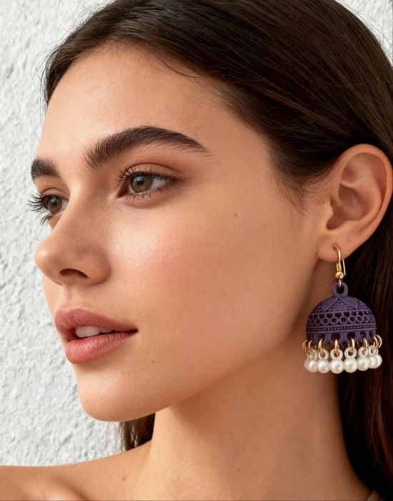 Close-up of a woman wearing a purple earring with pearl drops against a neutral background