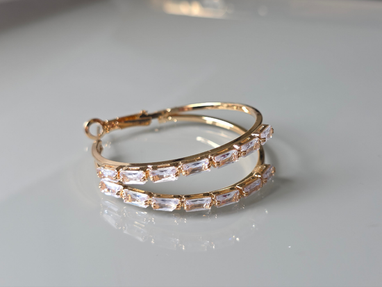 Gold hoop earrings with clear gemstones on a light gray background