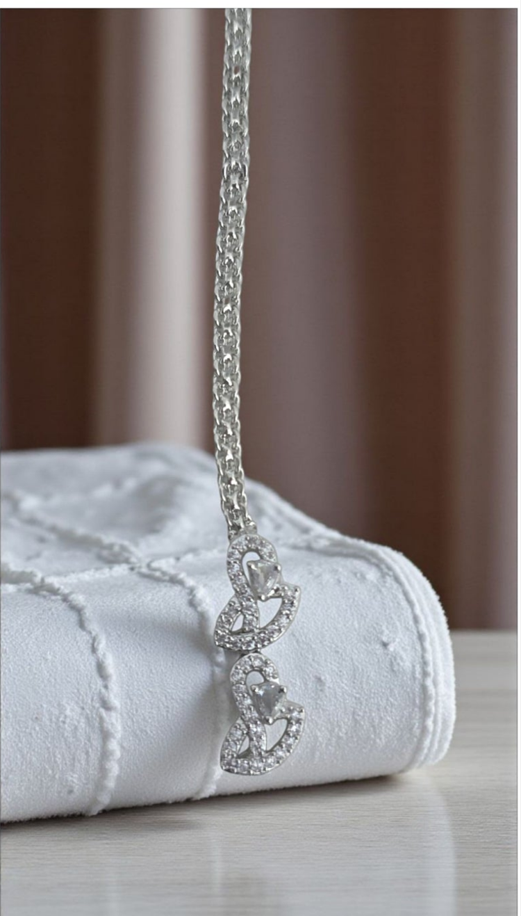 Silver necklace on a white textured surface with a blurred brown background