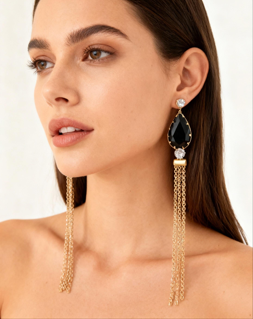 Woman wearing a pair of long, dangling earrings with a black gemstone and gold chain.