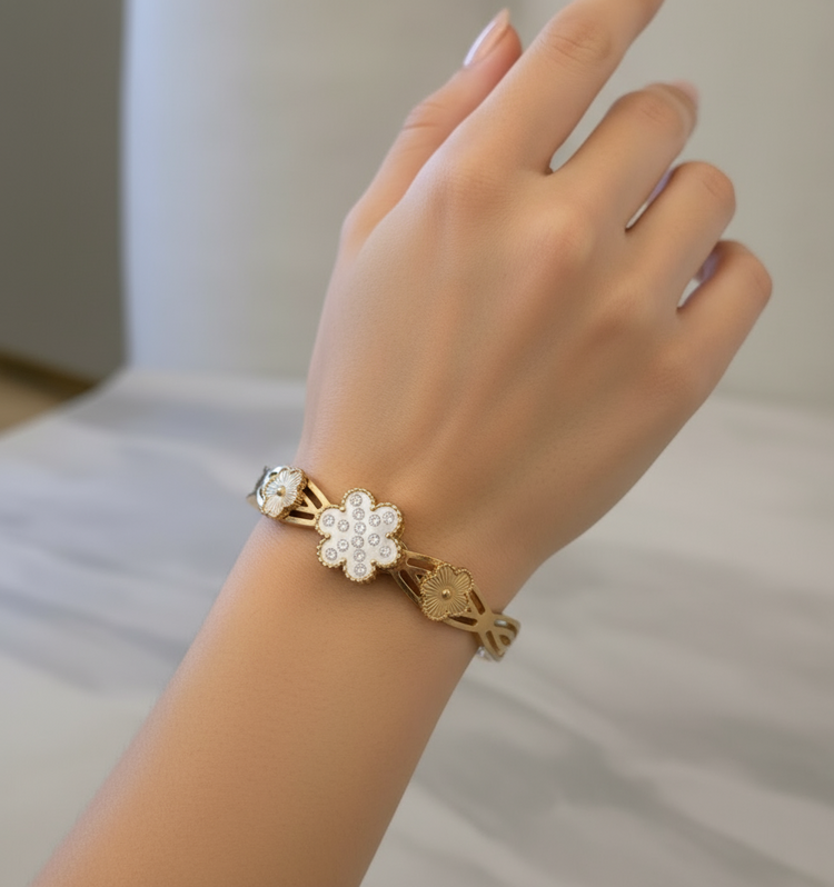 Gold bracelet with floral designs on a black stand against a light background
