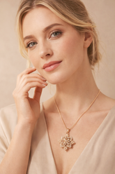 Woman wearing a gold necklace with a floral pendant against a beige background