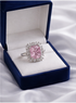 Pink diamond ring in a blue velvet box on a white fabric background