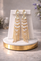 Gold tassel earrings on a white and gold stand with a blurred floral background