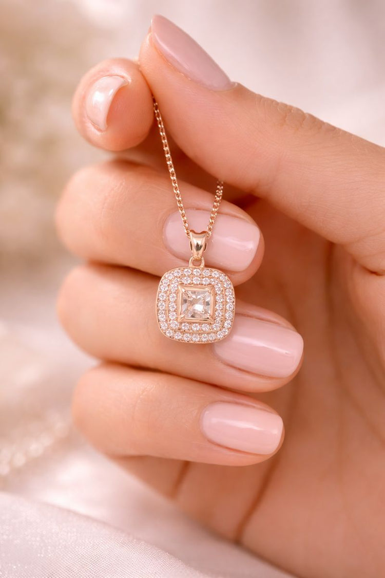 Rose gold necklace with a diamond pendant held by a hand with pink nail polish.