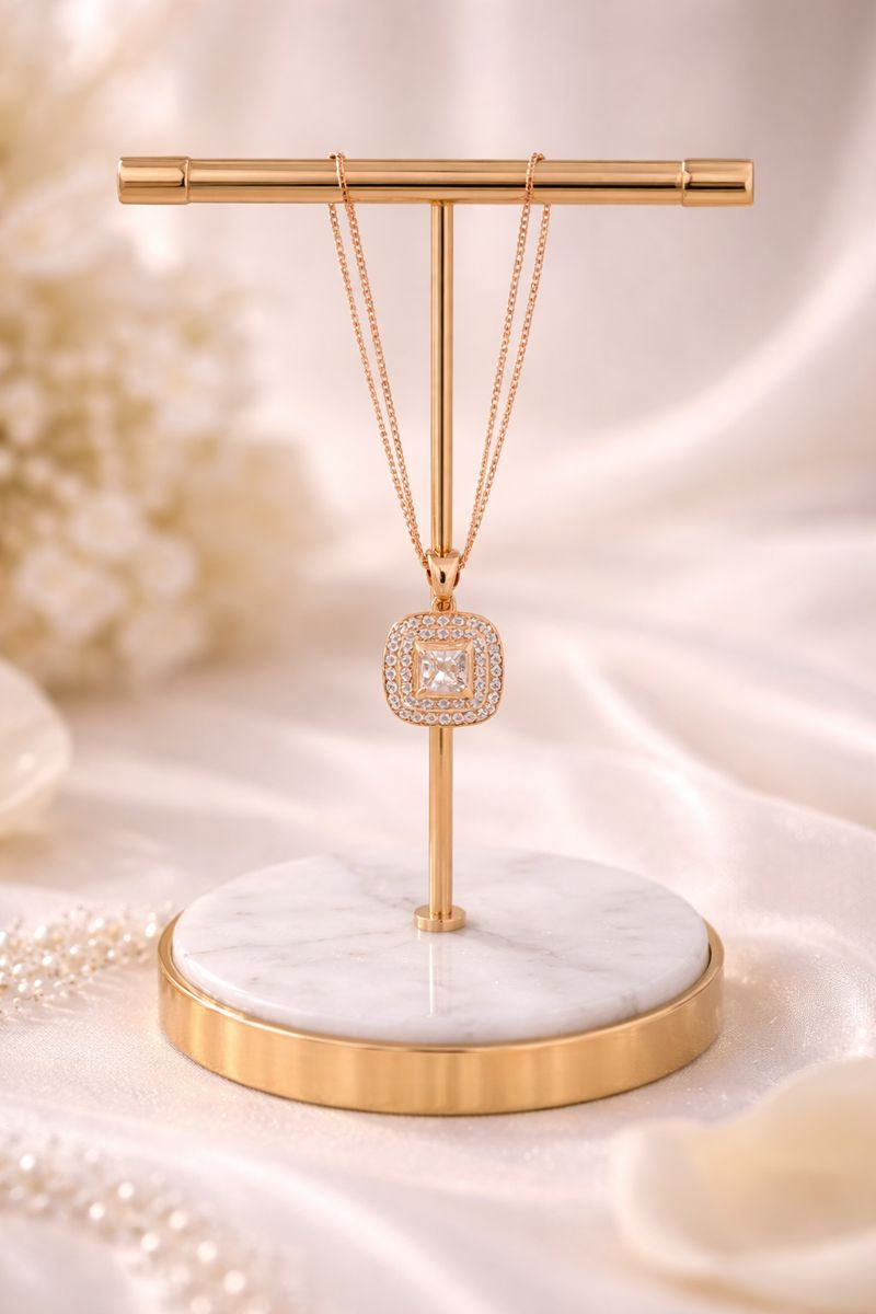 Necklace with a diamond pendant on a gold and marble stand against a soft, blurred background.
