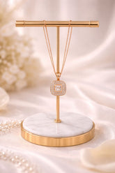 Necklace with a diamond pendant on a gold and marble stand against a soft, blurred background.