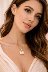 Woman wearing a necklace with a diamond pendant against a neutral background