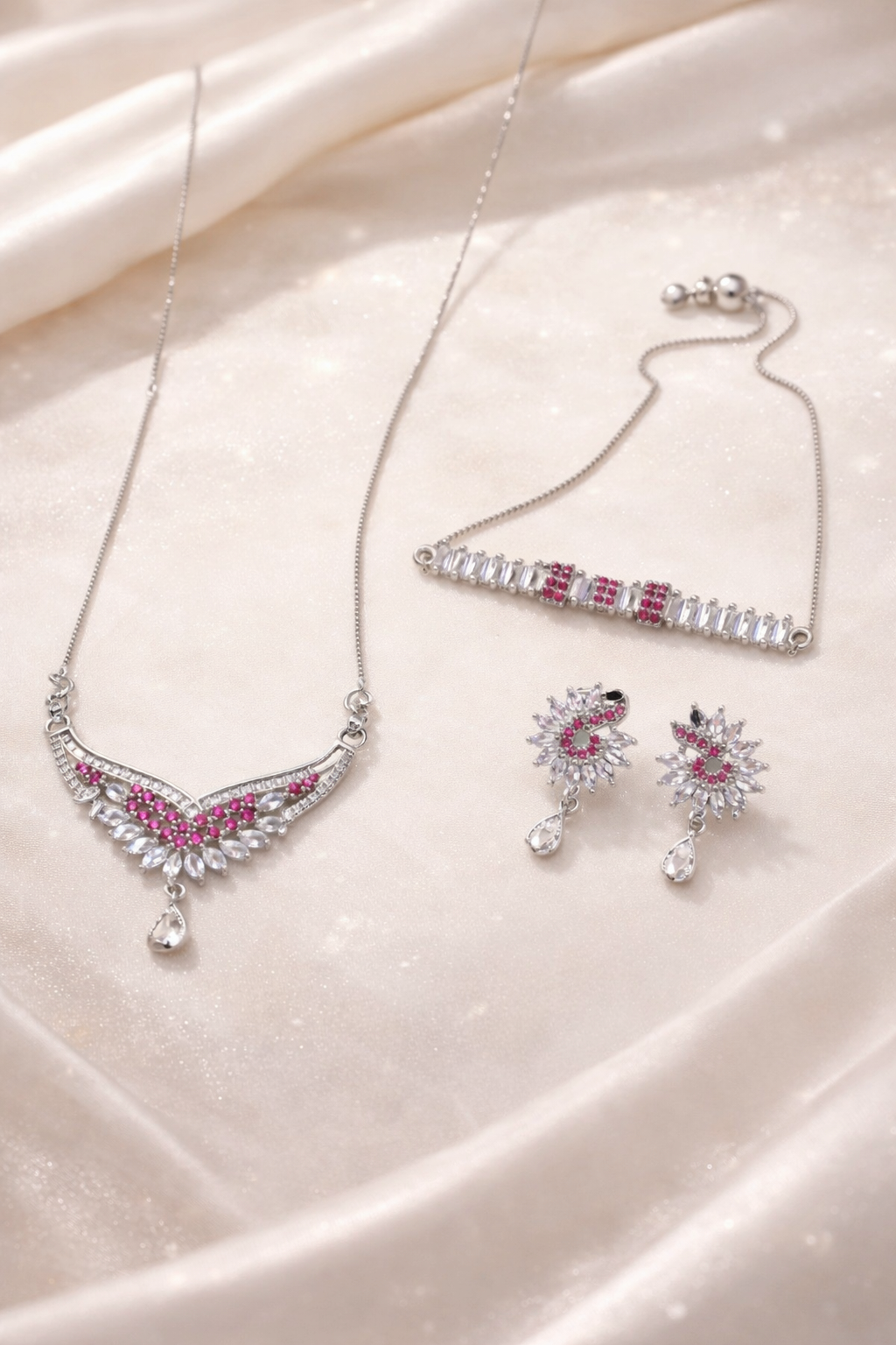 Silver jewelry set with pink gemstones on a soft fabric background