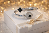 Silver bracelet with black stones on a white box with a bow, against a glittery gold background