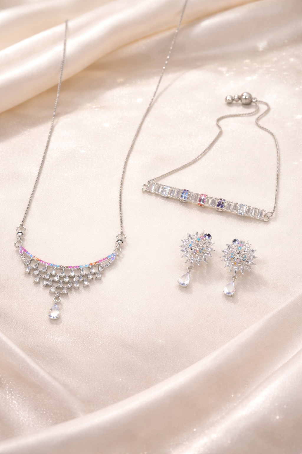 Silver jewelry set with necklace, bracelet, and earrings on a pink satin background