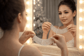 Woman trying on a diamond necklace in front of a mirror with lights.