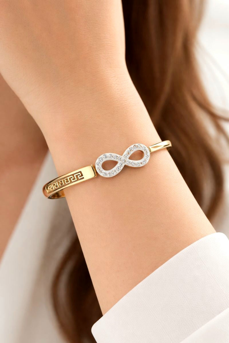 Gold bracelet with infinity design on a wrist against a neutral background