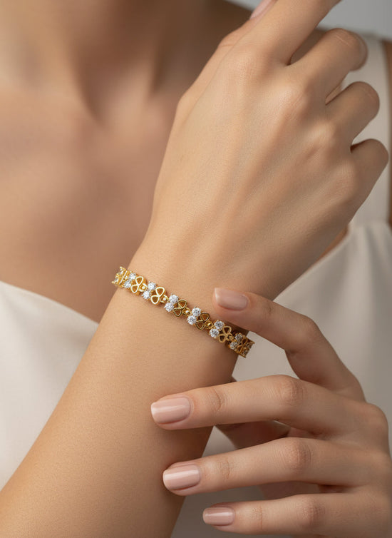 Gold bracelet with floral design on a wrist against a neutral background