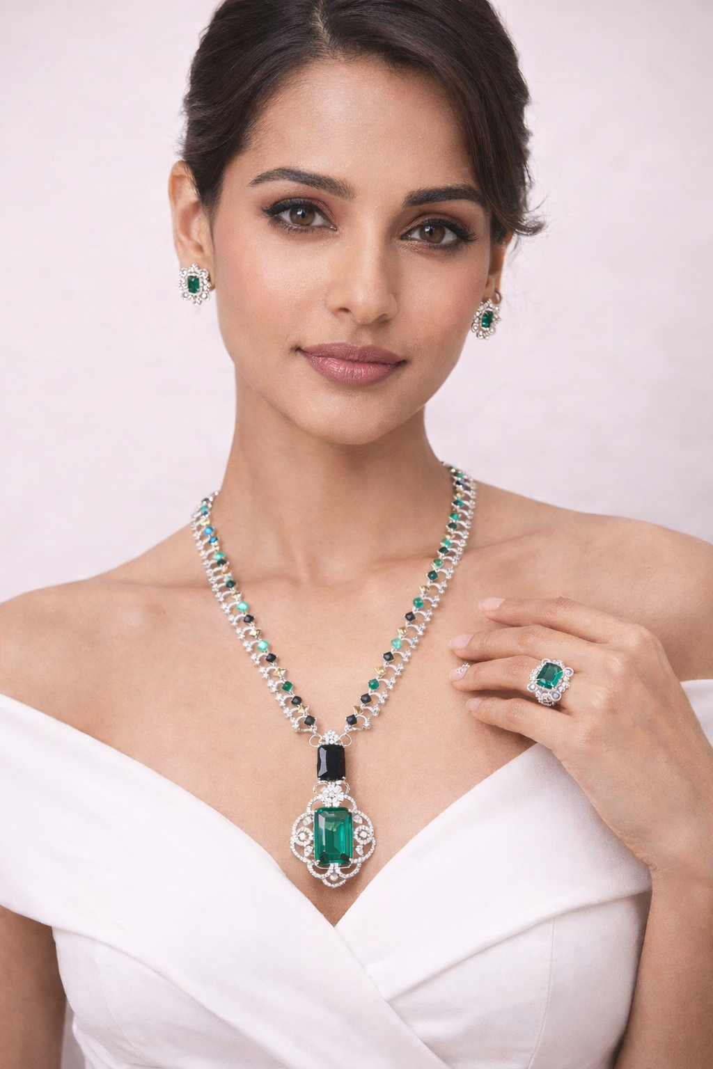 Woman wearing emerald jewelry including a necklace, earrings, and ring on a light pink background