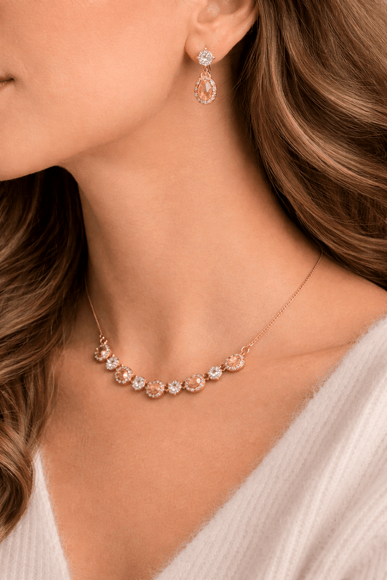 Close-up of a woman wearing a rose gold necklace and earrings with gemstones.