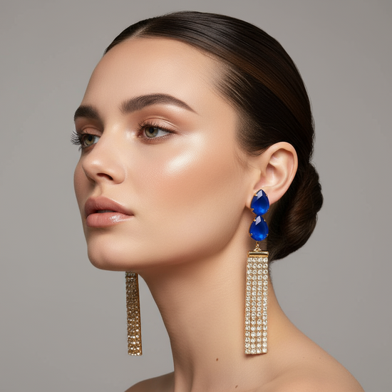 Pair of earrings with blue teardrop stones and gold accents on a gray background