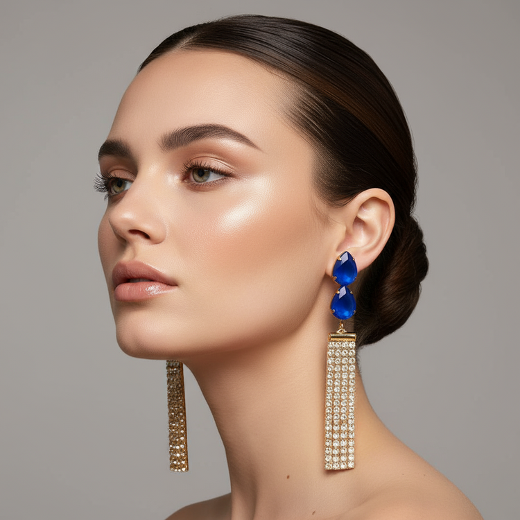 Pair of earrings with blue teardrop stones and gold accents on a gray background