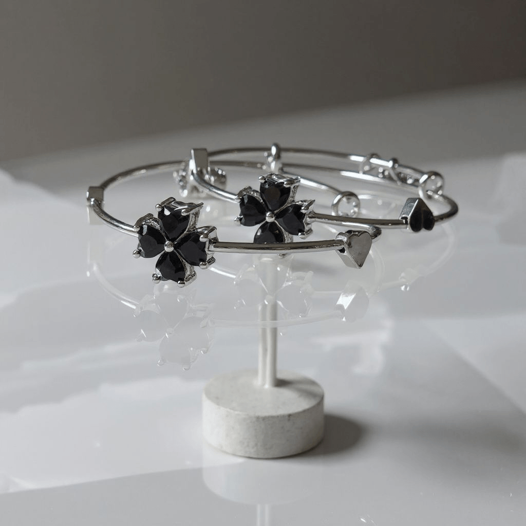 Silver bangles with black flower-shaped ends on a white stand against a light gray background